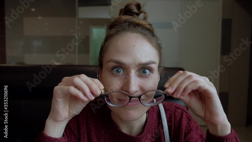 Funny young girl with glasses fool around sits in cafe and smile.