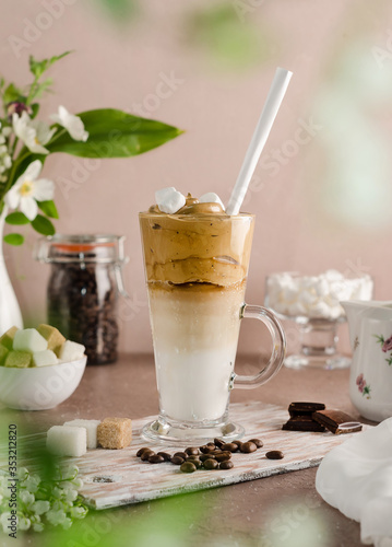 Cold coffee dalgon in a tall glass on a beige wooden background. Foam whipped with a mixer made of sugar, instant coffee and water in cold milk with ice. Korean and indian whipped coffee. photo