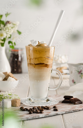 Cold coffee dalgon in a tall glass on a white wooden background. Foam whipped with a mixer made of sugar, instant coffee and water in cold milk with ice. Korean and indian whipped coffee.