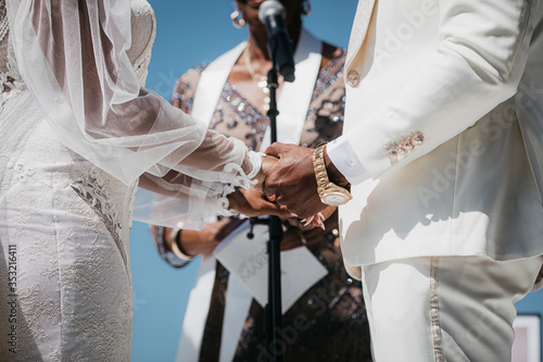 The marriage registrar is talking to groom and bride on wedding ceremony, close up photo. Bride and broom holding hands each other. Afro-american wedding