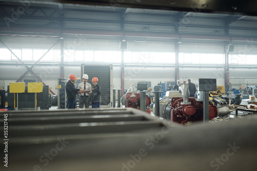 People in hardhats using tablet and discussing engineering project while working at compressor plant © pressmaster
