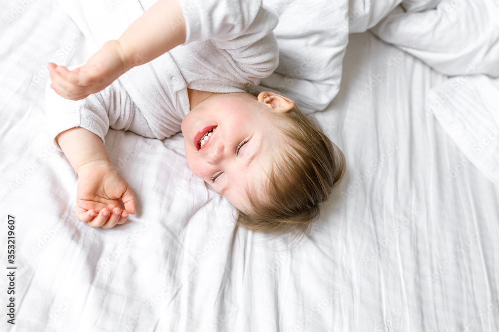 A small child close up lying on a white sheet in a bright room at home A small child close up lying on a white sheet in a bright room at home