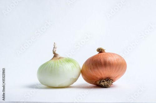 Two onions lie on a white background. One onion peeled  the other in the husk