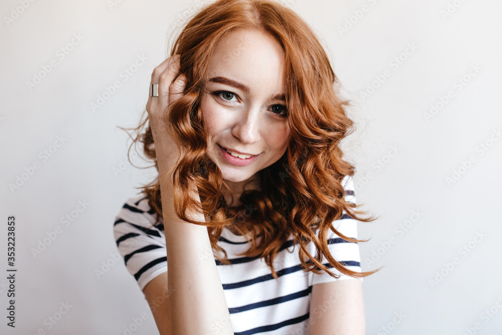 Ecstatic girl wears ring touching her ginger hair. Indoor portrait of inspired female model in casual outfit isolated on white background. Ecstatic girl wears ring touching her ginger hair. Indoor portrait of inspired female model in casual outfit isolated on white background.