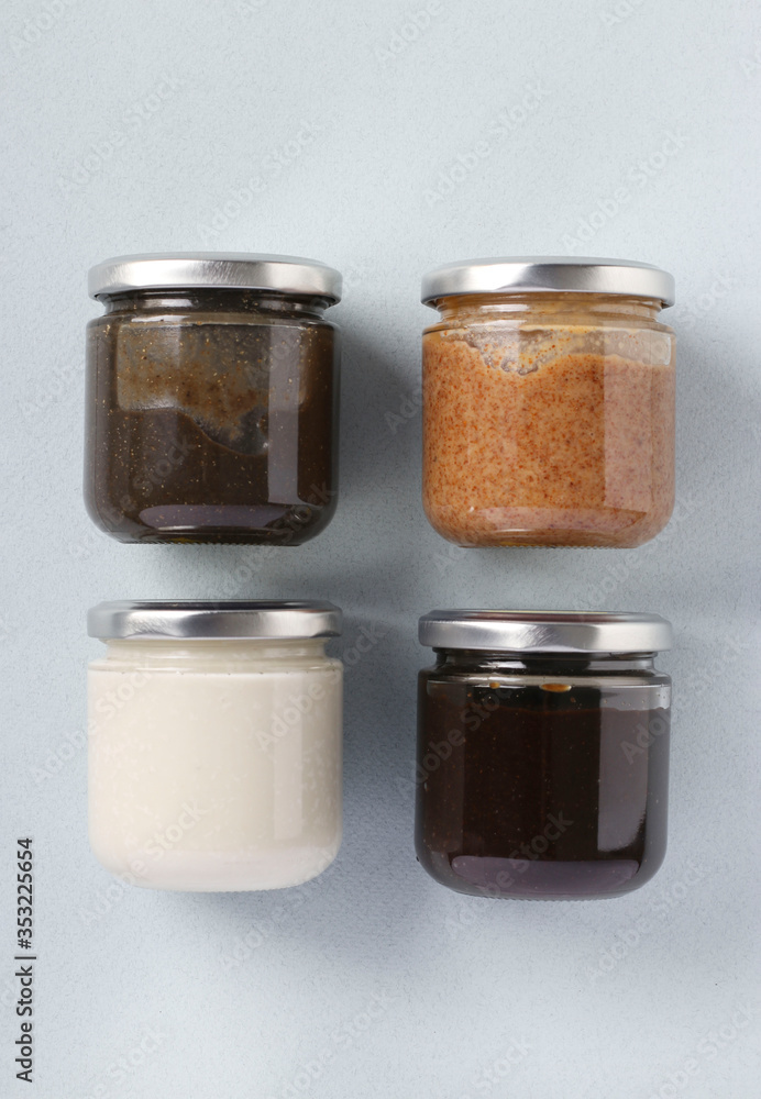 Vegan organic paste of flax seeds, milk thistle, peanuts and coconut in glass jars on light blue background, urbech, Vertical format, Top view Vegan organic paste of flax seeds, milk thistle, peanuts and coconut in glass jars on light blue background, urbech, Vertical format, Top view