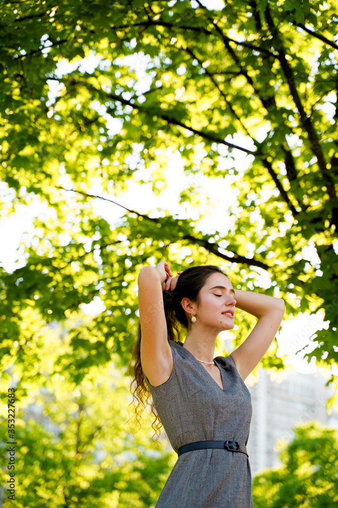 Relaxation and meditation lifestyle of young girl in green park. Vertical photo of beautiful girl who touches and correct her hair. Woman dresses casual style. Dreamily girl after quarantine Relaxation and meditation lifestyle of young girl in green park. Vertical photo of beautiful girl who touches and correct her hair. Woman dresses casual style. Dreamily girl after quarantine