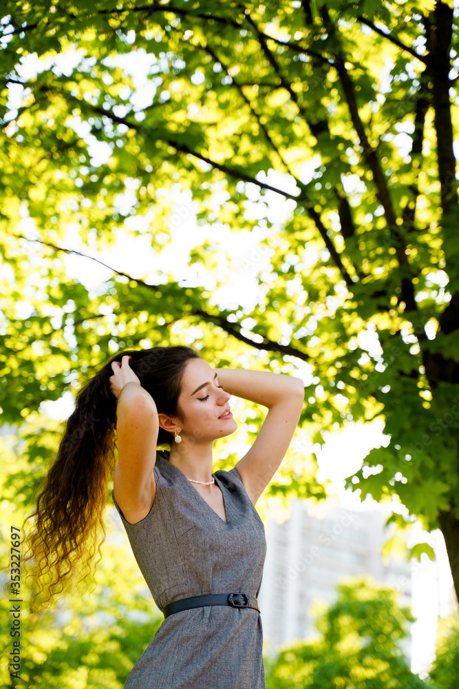 Relaxation and meditation lifestyle of young girl in green park. Vertical photo of beautiful girl who touches and correct her hair. Woman dresses casual style. Dreamily girl after quarantine Relaxation and meditation lifestyle of young girl in green park. Vertical photo of beautiful girl who touches and correct her hair. Woman dresses casual style. Dreamily girl after quarantine