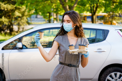 Girl holds 4 coffee in hands with gloves. One cup of coffee in hands. Delivery coffee by car. Girl courier in medical mask and gloves. 2+2 promotion. Advertise for coffee house. Safe delivery
