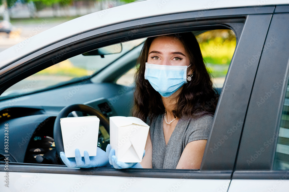 Young attractive girl in car in medical gloves and mask holds wok in box udon noodles with tempuru, shrimps, in hands and smiles. Udon noodles in white box delivery. 2 Wok box udon advertise 1+1.
