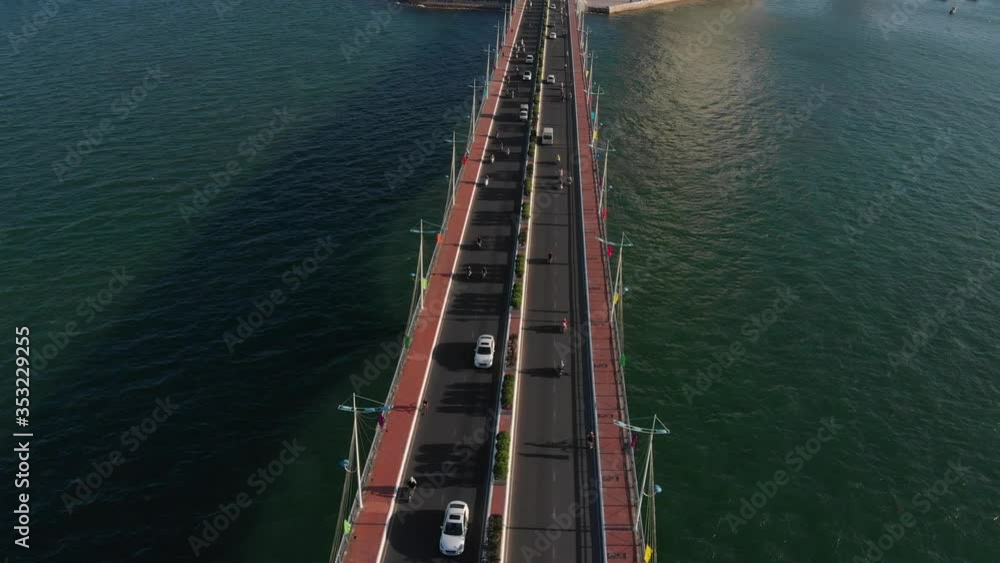 Shooting Aerial unmanned flight from top view of the city bridge with cars and motorbikes against the backdrop of the beautiful sea of the ocean and large town buildings. Bridge and city highway. Shooting Aerial unmanned flight from top view of the city bridge with cars and motorbikes against the backdrop of the beautiful sea of the ocean and large town buildings. Bridge and city highway.