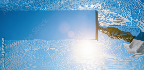 Fotografi Window cleaner cleaning window with squeegee and wiper on a sunny day with a bri