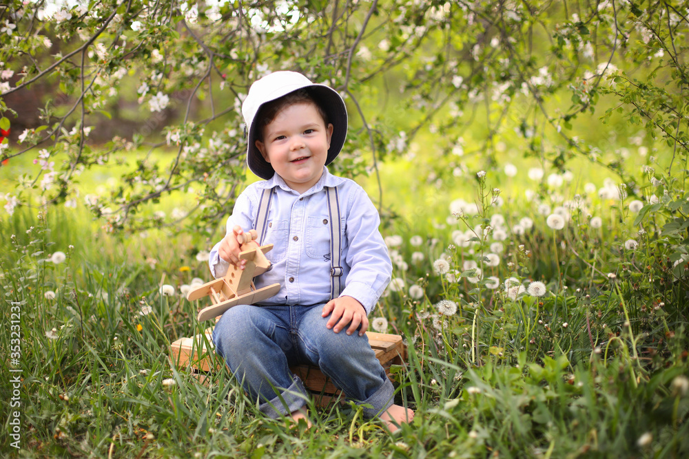Little cute blond boy playing with a wooden plane in the summer park on the grass on a sunny day, focus on the child, blurred background Little cute blond boy playing with a wooden plane in the summer park on the grass on a sunny day, focus on the child, blurred background
