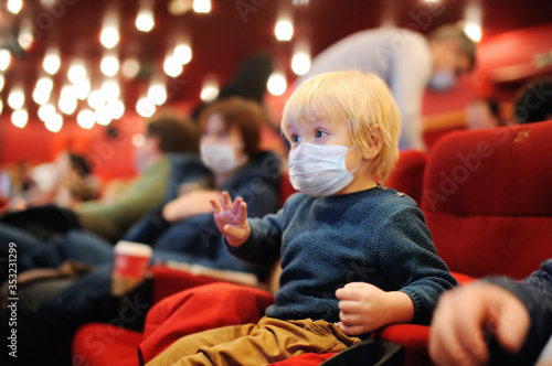 Cute toddler boy wearing face mask watching cartoon movie in the cinema after quarantine. Lifting virus lockdown. Social distancing restrictions remain.