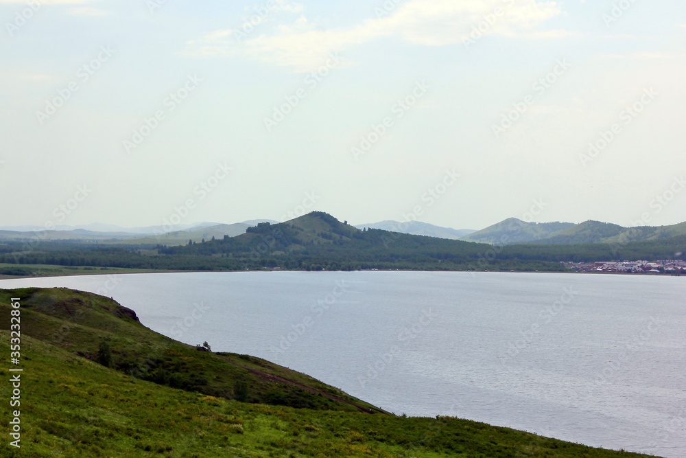 Panoramic view. A lagoon with a clean mountain lake in the midst of majestic mountains in a haze of fog. Green hills in the fog
