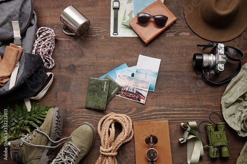 Above view of nature photos and passports among hiking stuff on dark wooden table, active vacation flat lay