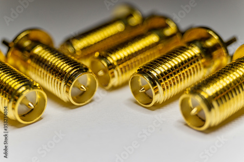 Close-up of symmetric aligned gold plated SMA male connectors electronics components in partial focus white background