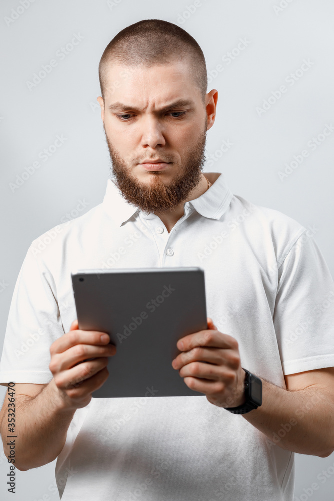 Portrait of a handsome bearded man in a white t-shirt working in a tablet. isolated, emotions Portrait of a handsome bearded man in a white t-shirt working in a tablet. isolated, emotions