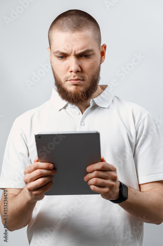 Portrait of a handsome bearded man in a white t-shirt working in a tablet. isolated, emotions
