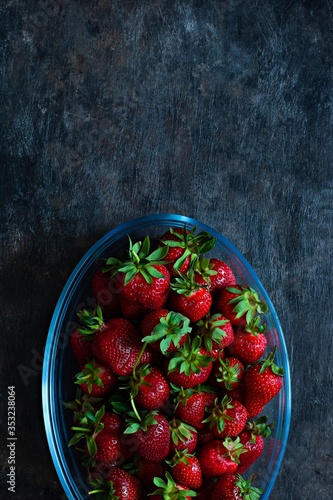 Fresh ripe strawberries in a glass dish on a dark background, top view.