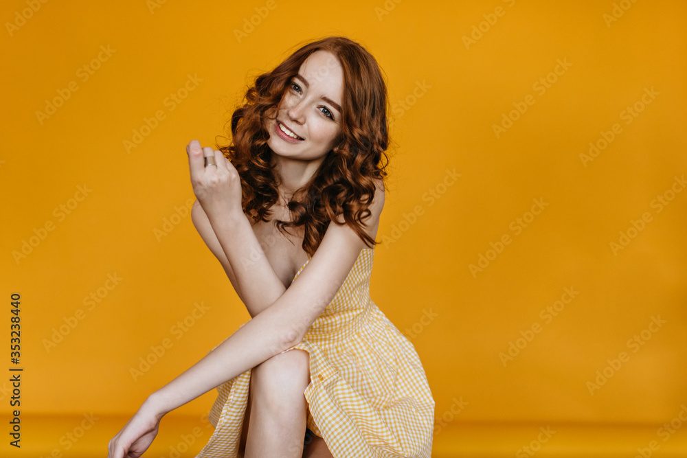 Fototapeta premium Slim stunning lady in yellow dress posing on orange background. Indoor photo of adorable ginger girl in bright outfit.