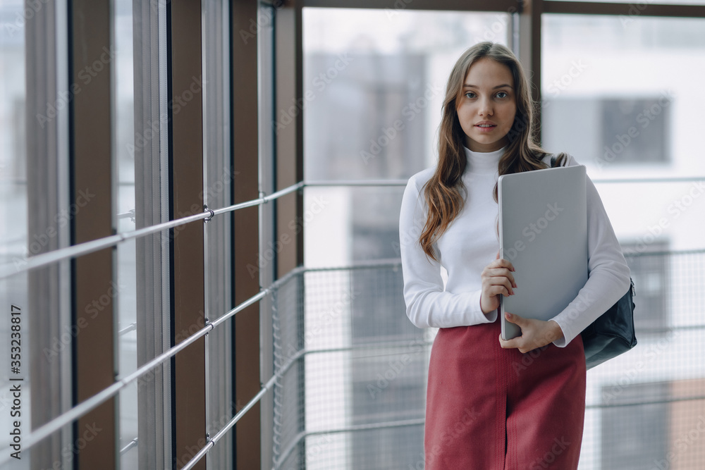 attractive girl walks in a bright corridor with laptop and things in airport terminal or office. travel atmosphere or alternative work atmosphere. freelancer student travels to business meeting. attractive girl walks in a bright corridor with laptop and things in airport terminal or office. travel atmosphere or alternative work atmosphere. freelancer student travels to business meeting.