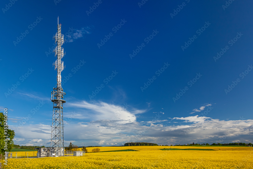 Wieża radiowa na polu żółtego rzepaku i tle niebieskiego nieba. - obrazy, fototapety, plakaty 