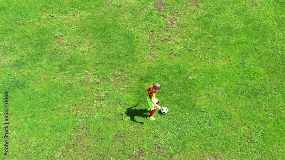 Boy kicking football on the sports field. Child playing soccer on green grass. View from above. Drone view. Boy kicking football on the sports field. Child playing soccer on green grass. View from above. Drone view.