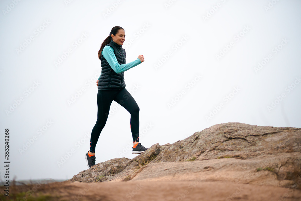 Beautiful Smiling Woman Running on the Mountain Trail at Cold Autumn Evening. Sport and Active Lifestyle.