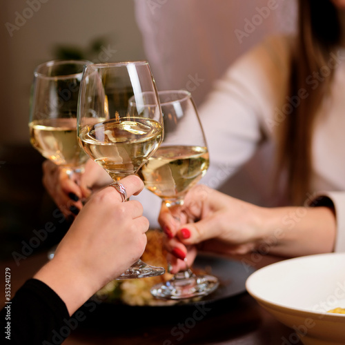 female friends - hands clinking white wine glasses  restaurant or bar on background  close up view. evening  celebration and holidays concept