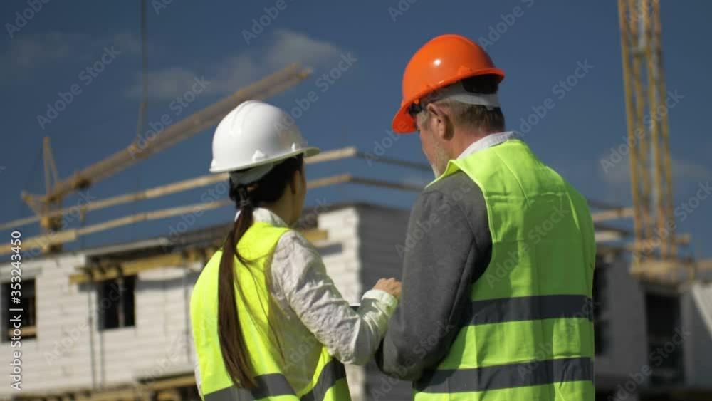 Man and young woman in helmets on the background of a house under construction. They discuss working issues. Man and young woman in helmets on the background of a house under construction. They discuss working issues.