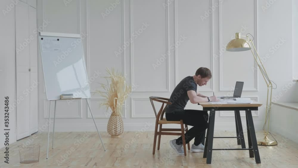 A man in a stylish loft works with documents. A young man works sitting at a table. A man crumpled a sheet of paper and throws it into the urn with a displeased look. A man in a stylish loft works with documents. A young man works sitting at a table. A man crumpled a sheet of paper and throws it into the urn with a displeased look.