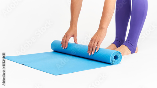 Close-up hands and feet of a woman in sportswear, rolling out a Mat for sports.