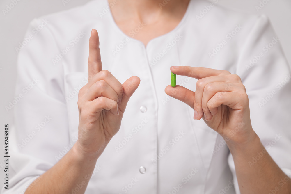 A girl doctor in a white robe holds a capsule pill with a closeup medicine for the disease. A girl doctor in a white robe holds a capsule pill with a closeup medicine for the disease.