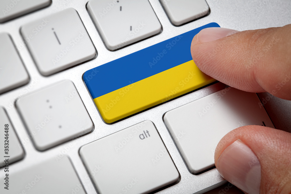 Online International Business concept: Computer key with the Ukraine flag on it. Male hand pressing computer key with Ukraina flag. - obrazy, fototapety, plakaty 