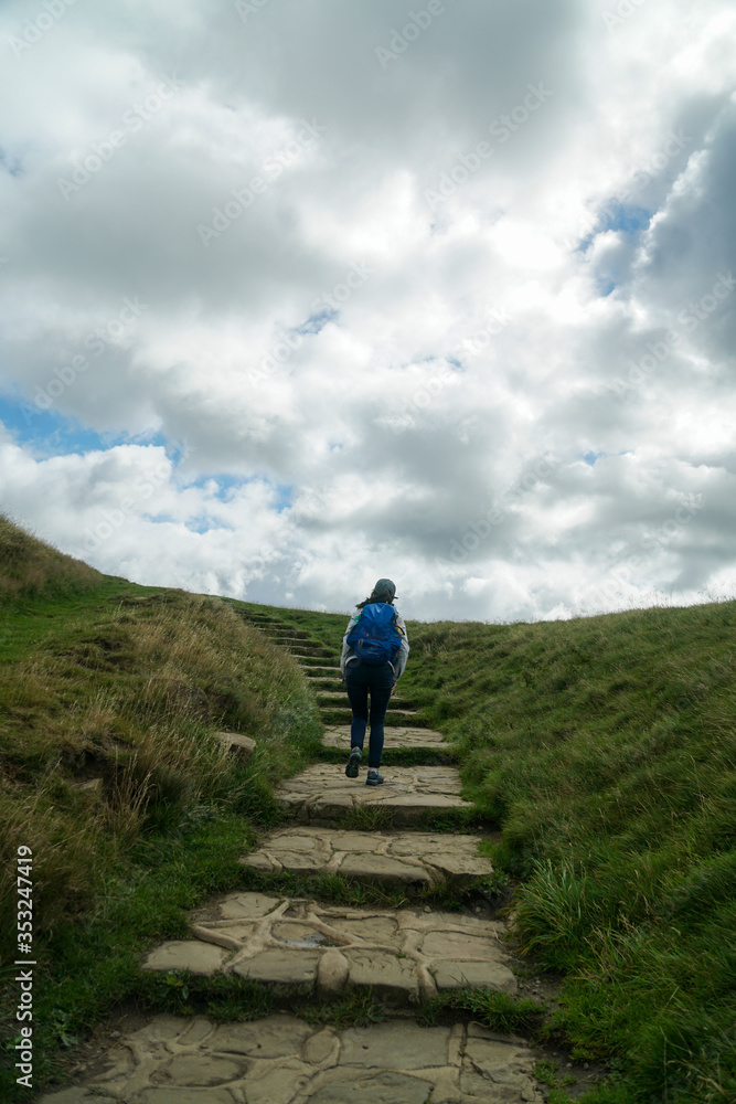 A female hiker walking up the hill with a blue backpack in Peak District National Park in the UK