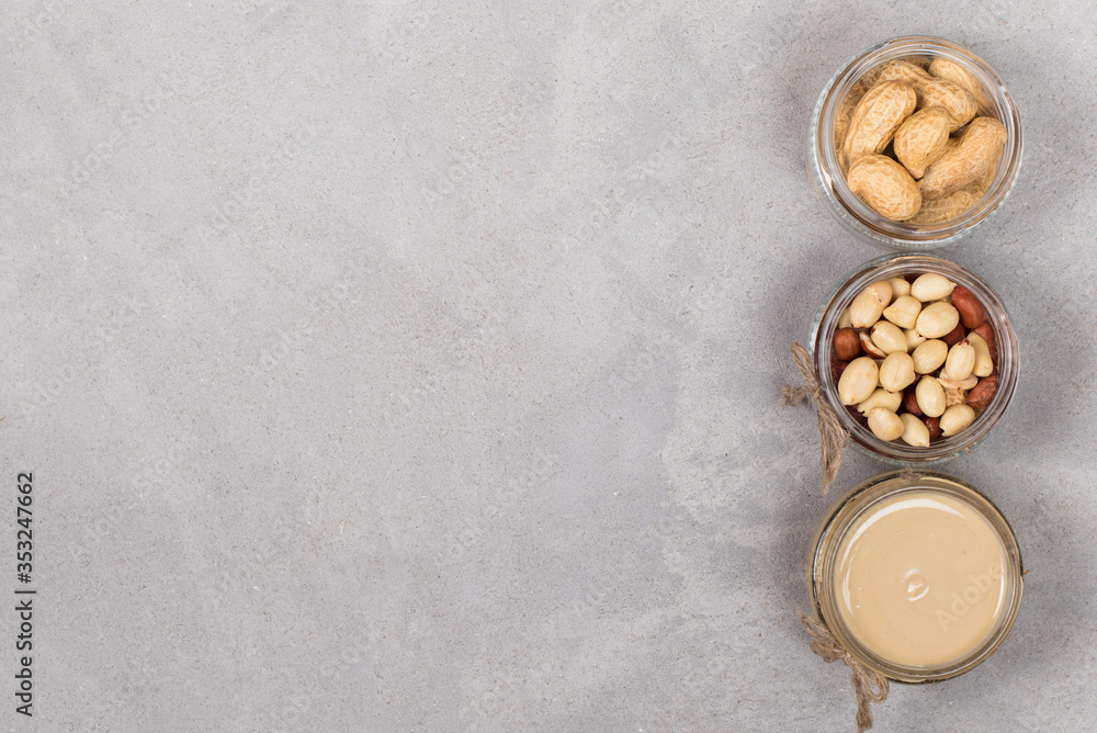 Peanut paste, peeled peanuts, peanuts in husks in jars in rustic style on a light gray background top view copy space