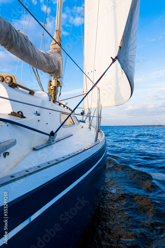 Blue yacht sailing in the river at sunset, Norway. A view from the deck to the bow and sails. Clear blue sky. Sport and recreation theme photo