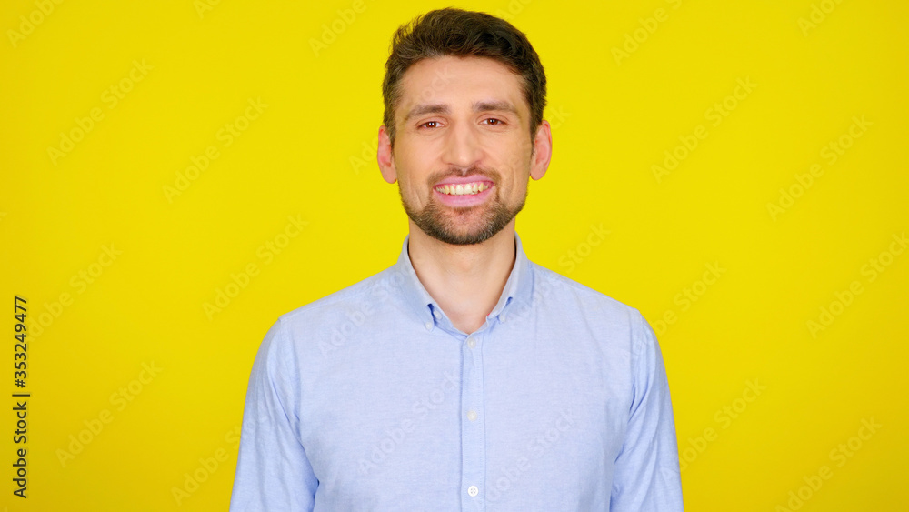Handsome bearded man in a light blue shirt smiles. Businessman looking at the camera on a yellow background with place for text Handsome bearded man in a light blue shirt smiles. Businessman looking at the camera on a yellow background with place for text