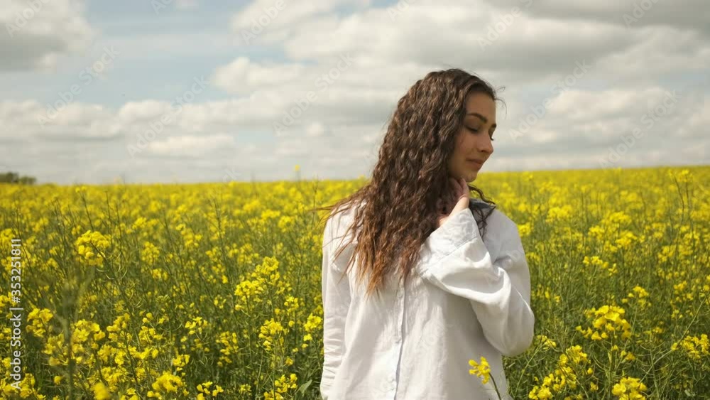 Cheerful girl of Caucasian appearance in rapeseed. Walks across the field in yellow flowers Cheerful girl of Caucasian appearance in rapeseed. Walks across the field in yellow flowers