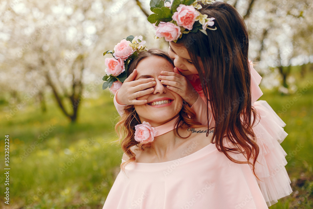 Naklejka premium Pretty mother with daughter. Family in a spring park. Woman in a pink dress. Child with a flowers