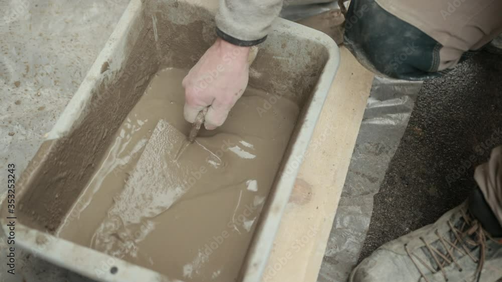A Man's Hand With Spatula Mixes Liquid Solution In Wheelbarrow For Construction Consisting Of Water, Cement, Gypsum And Sand. Concept Of builders, People At Work A Man's Hand With Spatula Mixes Liquid Solution In Wheelbarrow For Construction Consisting Of Water, Cement, Gypsum And Sand. Concept Of builders, People At Work