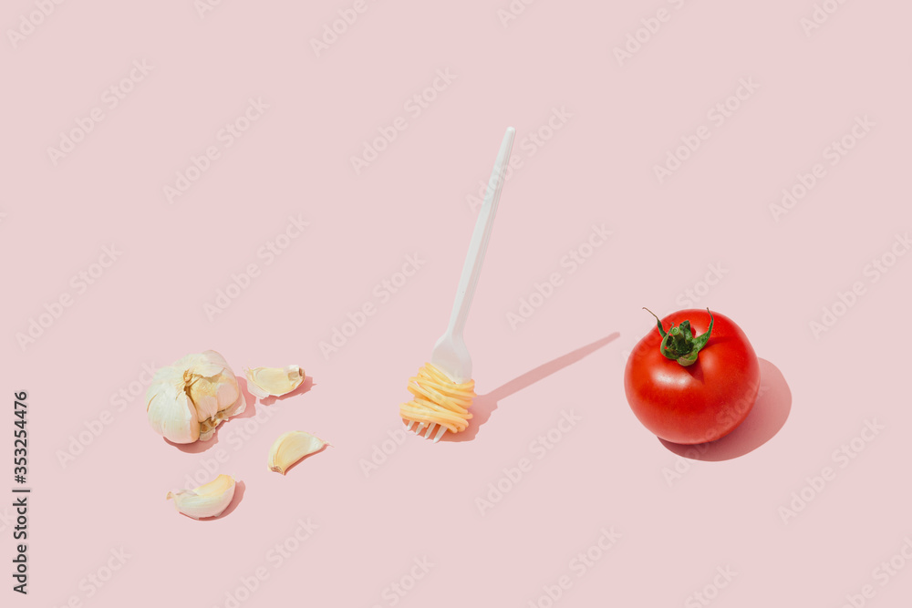 Minimal food concept with fork with spaghetti pasta, tomato and garlic against pastel pink background. Minimal food concept with fork with spaghetti pasta, tomato and garlic against pastel pink background.