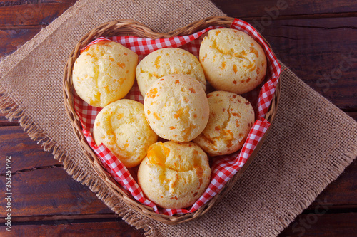 homemade cheese bread, traditional Brazilian snack, in a heart-shaped basket on a rustic kitchen table photo