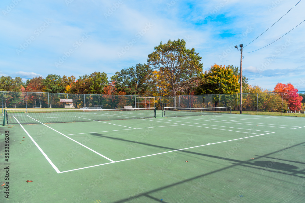 Deserted tennis court with colourful deciduous trees in background in a public park on a sunny autumn morning