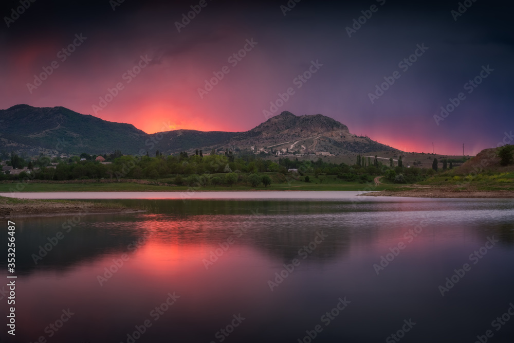 Amazing sunset on a beautiful mountain lake. Colorful lilac, pink, purple sunset sky is reflected in the mirror surface of the lake. Beautiful quiet evening in the mountains.