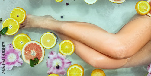 Woman relaxing in bath with orange, flowers.