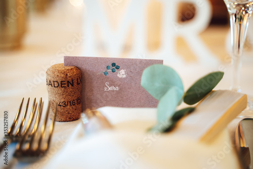 Closeup of label with name of guest in cork stand. Blurred elegant wedding table setting. Wedding day concept.