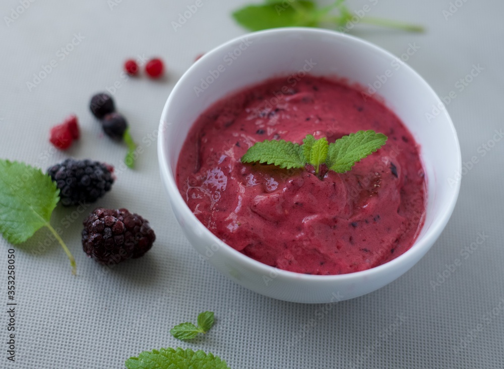 Homemade berry and mint ice cream in white bowl. Strawberries, blueberries, blackberries, and raspberries frozen and mint leaves on background. Fresh and healthy recipe Homemade berry and mint ice cream in white bowl. Strawberries, blueberries, blackberries, and raspberries frozen and mint leaves on background. Fresh and healthy recipe