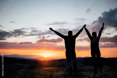 Young backpacker hiker couple enjoying relaxing mountain hike at sunset.Active hiking camping trip vacation in nature.Climbing up to the mountain top.Teamwork,success,challenge completion concept
