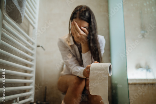 Sad woman on the toilet with toilet paper,suffering from abdominal pain.Female health problem with digestion and reproductive system.Constipation /menstrual cramps.Gluten/lactose intolerance symptoms